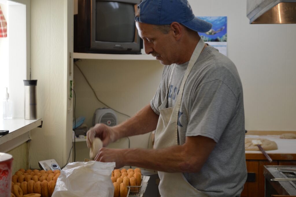 Chris Maville adding cinnamon powder to donuts.